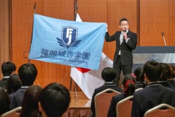 通信制高校　入学式　校長　校章　旗　舞台　マイク　礼服　スーツ